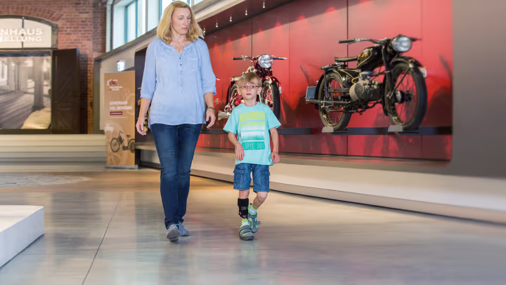 Mother and son visiting a motorcycle exhibition. The boy is wearing the WalkOn Reaction junior, a dynamic ankle-foot orthosis from Ottobock	