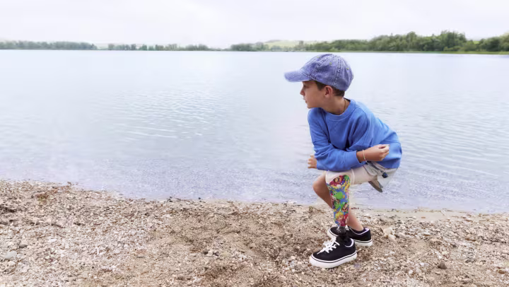 A boy throws stones into the water with his Maverick junior prosthetic foot.
