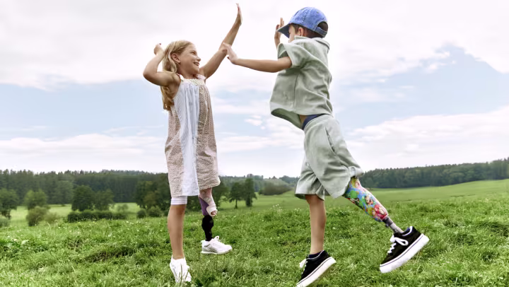 A boy with a prosthesis and a girl with a prosthesis jump up and high-five each other.