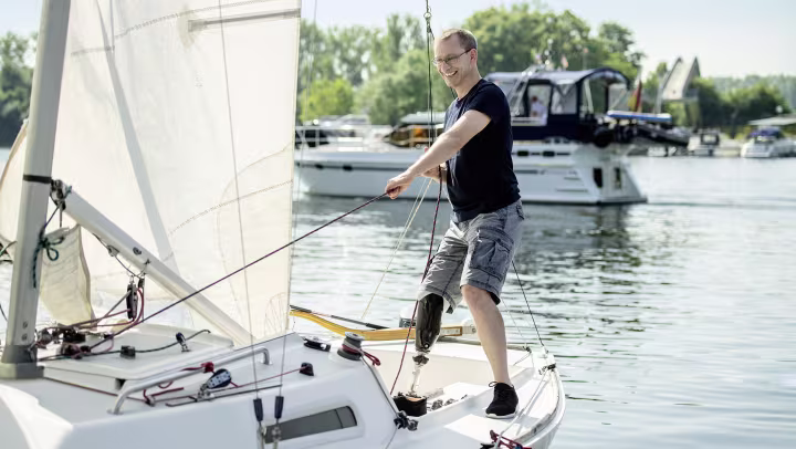 Peter is standing on the sailboat raising the sail.