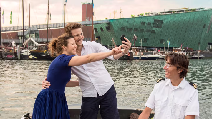 Marije and her boyfriend stand in the bow of a tourist boat, taking selfies with a smartphone.