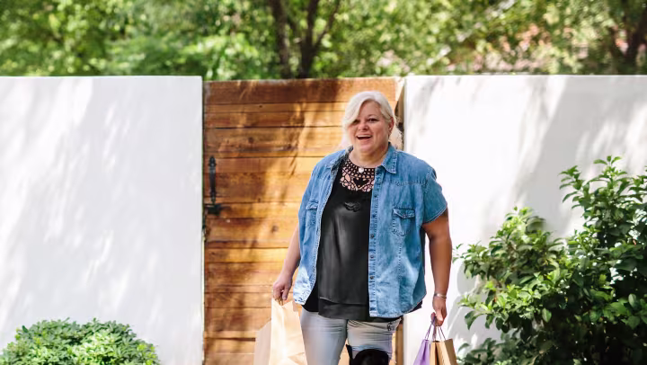 Diana wears her Meridium prosthetic foot as she walks up the uneven path to her house with shopping bags. 