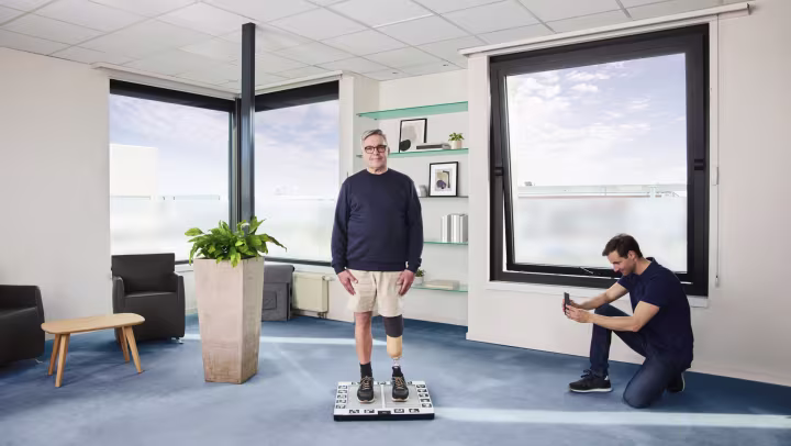 A patient with a prosthetic foot standing on the Ottobock lazar posture plate, with a technician monitoring the data on a mobile device. 