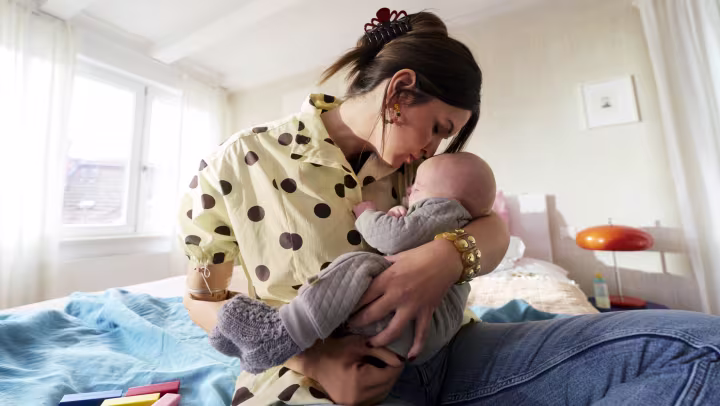 Prothesenanwenderin hat ihr Baby im Arm und küsst es auf die Stirn.