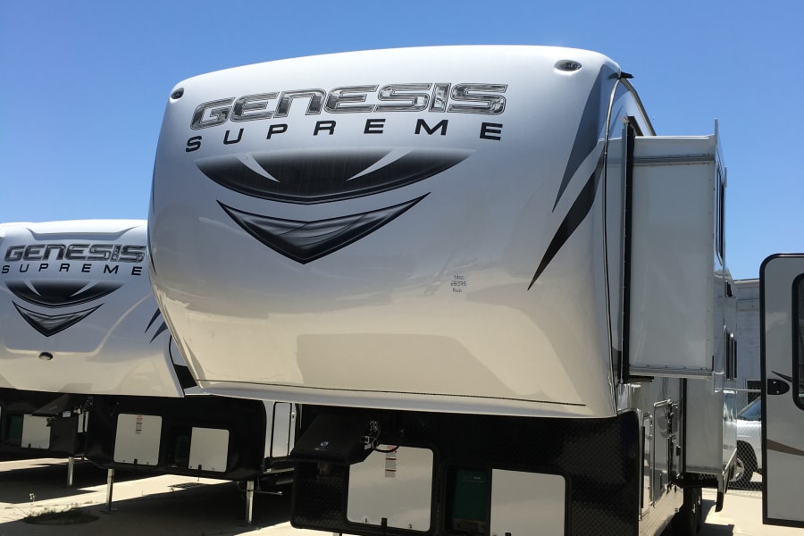 Two white Genesis Supreme fifth-wheel RVs parked on a sunny lot under a blue sky, ready for adventure. Explore options for your next rv rental.