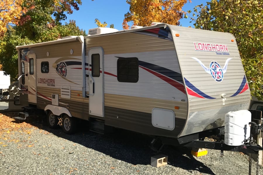 Longhorn Texas Edition RV rental parked outdoors, surrounded by vibrant fall trees and blue sky. Ideal for autumn camping.