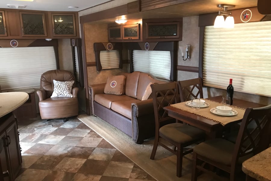 This RV rental's inviting living area includes a brown sofa, dining setup, and recliner, ready for travelers.