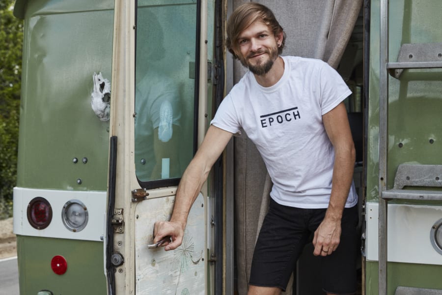 Smiling man standing in the doorway of a unique green vintage RV, ready for your next RV rental adventure.