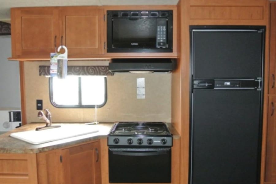 Kitchen area with microwave,  stove , gas fridge, storage and double sink