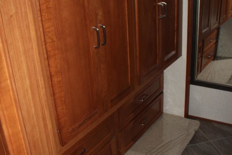 RV rental storage: Detailed wooden wardrobe with multiple cabinet doors, drawers, and a mirrored closet for ample RV organization.