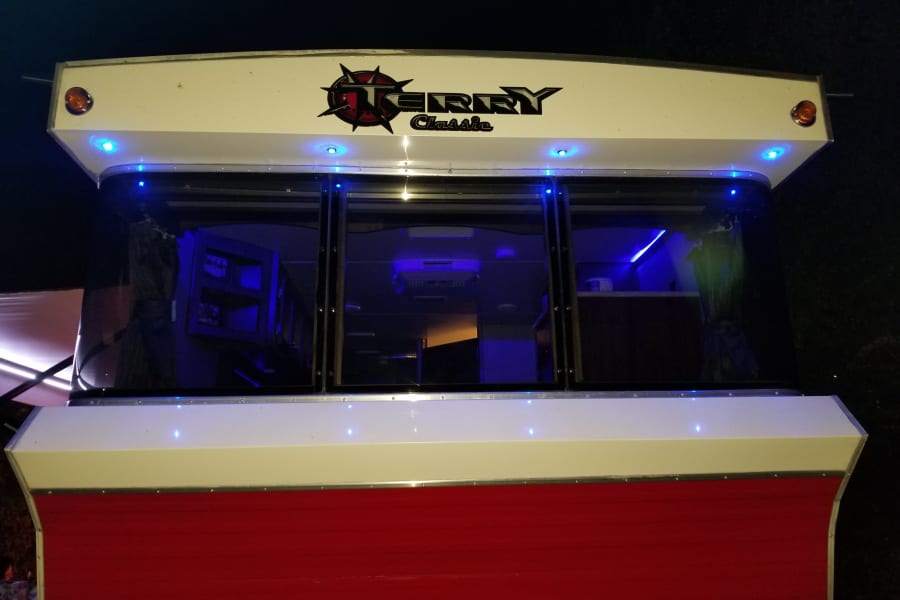 Night shot of an RV rental with blue interior and exterior lights. Features red and white exterior, Gerry Classic logo.
