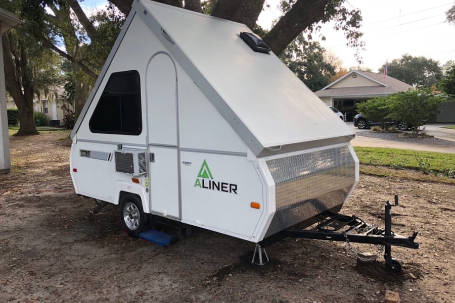 White A-Liner "Scout" A-frame pop-up camping trailer, a popular RV rental option, parked outdoors.