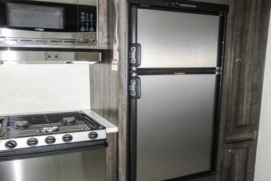 This RV rental features a modern kitchen with stainless steel microwave, range, and Dometic refrigerator, ready for your next trip.