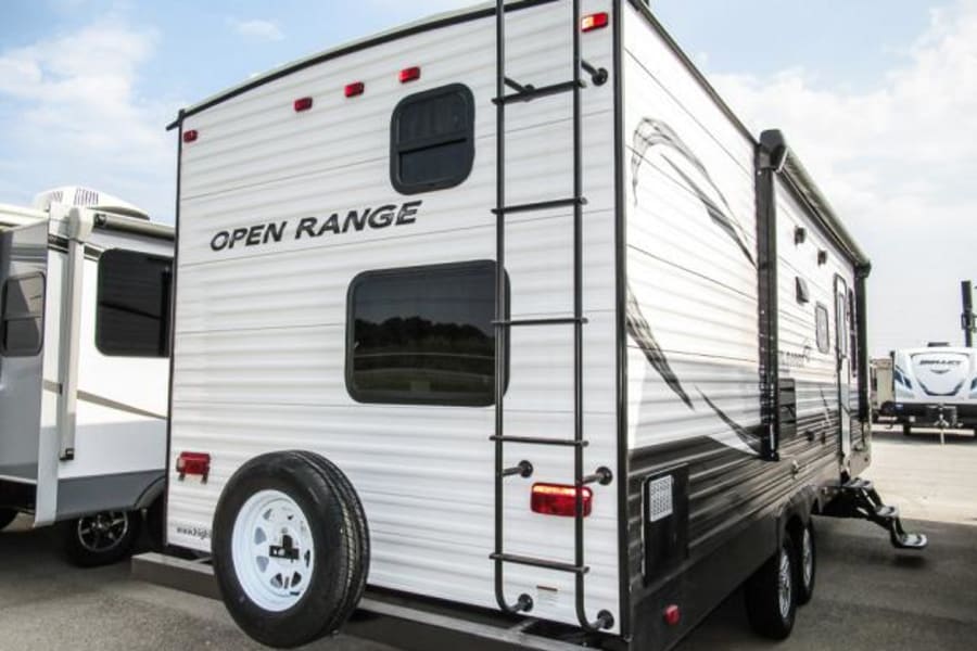 Rear view of a white Open Range travel trailer RV, perfect for your next RV rental or camping trip. Ladder & spare tire visible.