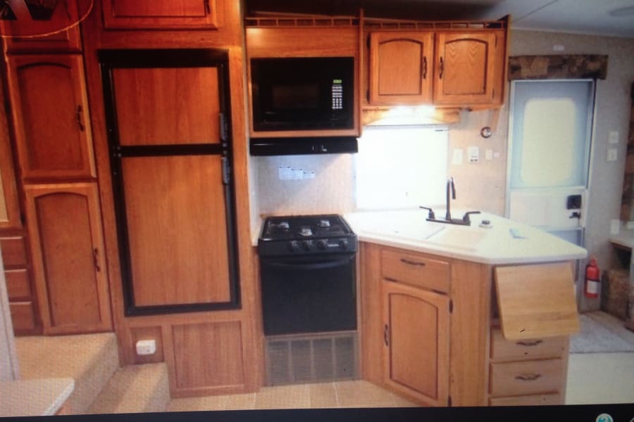 Compact RV rental kitchen showcasing a fridge, microwave, stove, sink, and wooden cabinetry.