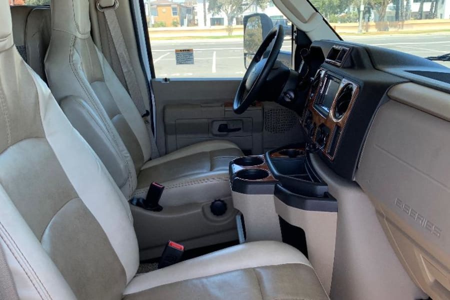 Step inside this spacious RV rental! View of the front cabin with two-tone seats, dashboard, and a clear street view.