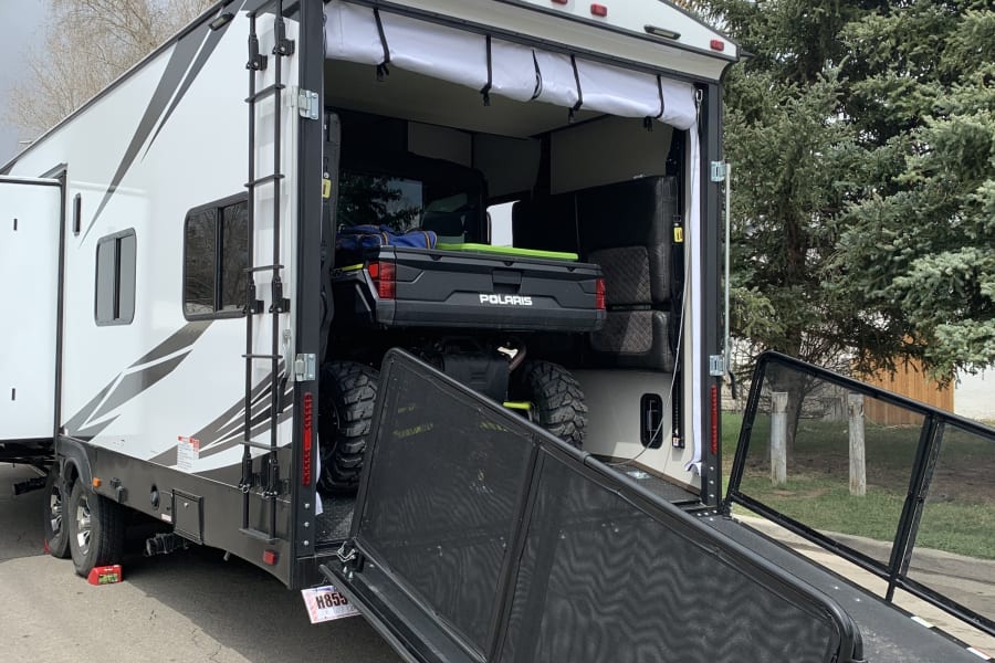 This RV rental, a toy hauler, has its rear ramp down, revealing an ATV inside. The back also features a screened patio.