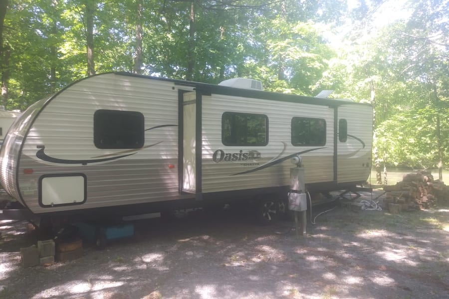 Experience nature with this spacious Oasis by Shasta RV rental parked at a tranquil, tree-lined campsite by the water.