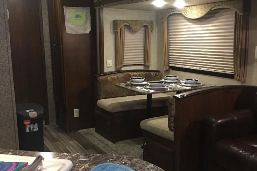 This RV rental interior offers a comfortable dining booth, living room seating, and practical kitchen counter for travelers.