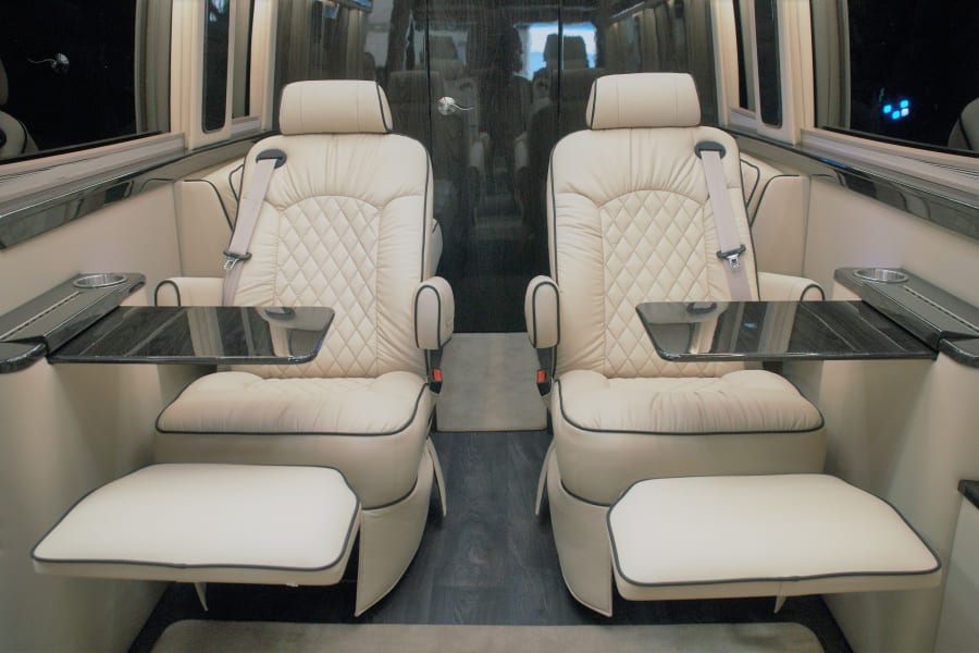 Premium RV rental interior: two plush captain's chairs with diamond stitching, integrated tables, and footrests for comfort.