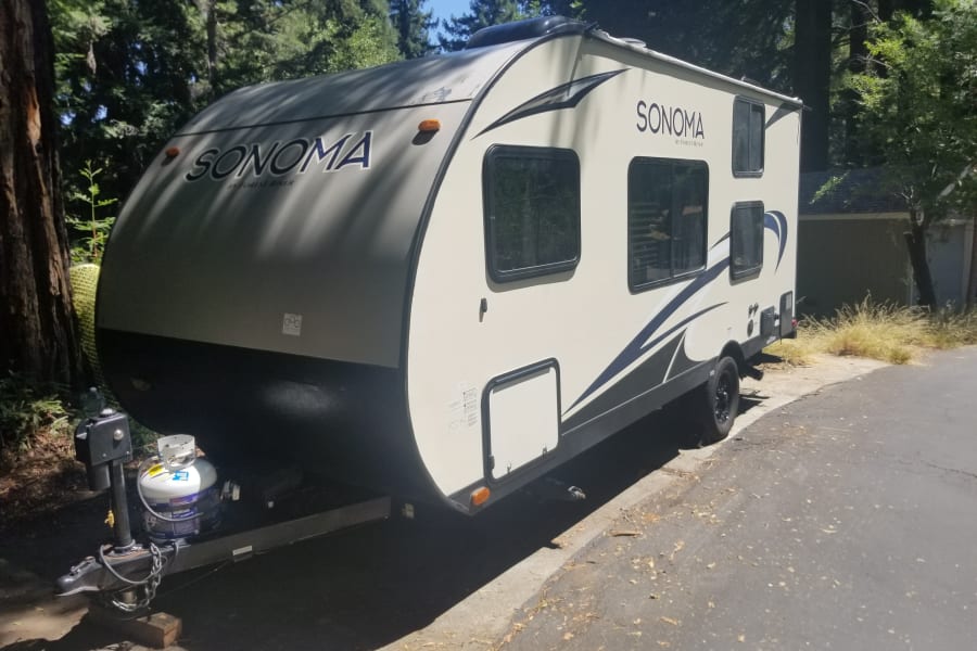 A light-colored Sonoma travel trailer RV rental, parked outdoors under a sunny sky with trees.