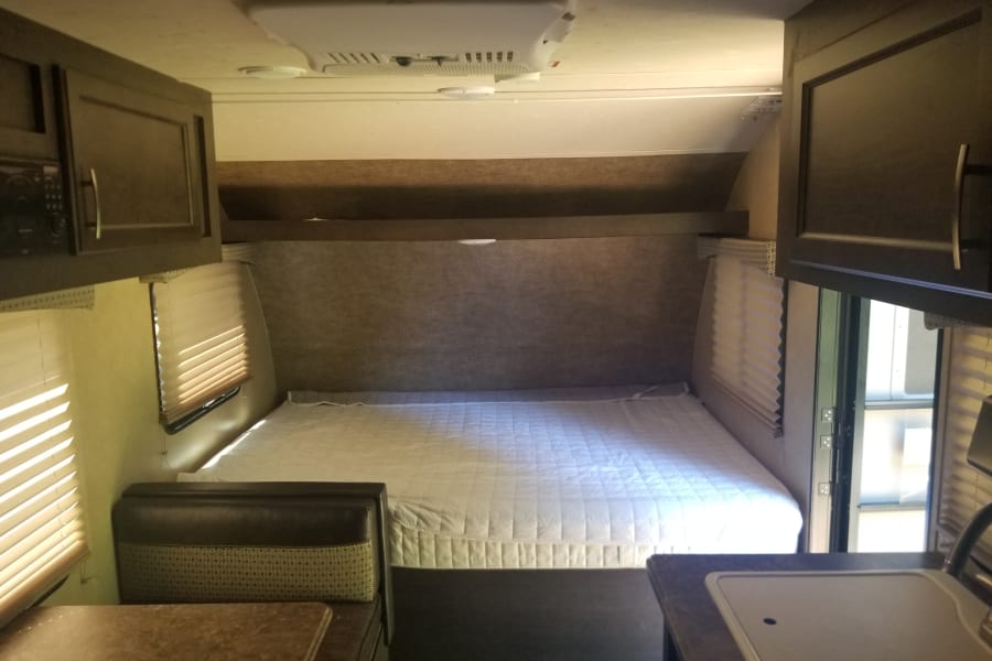 RV rental interior featuring a large bed, dining nook, and compact kitchen with a sink. Comfortable living on the road.