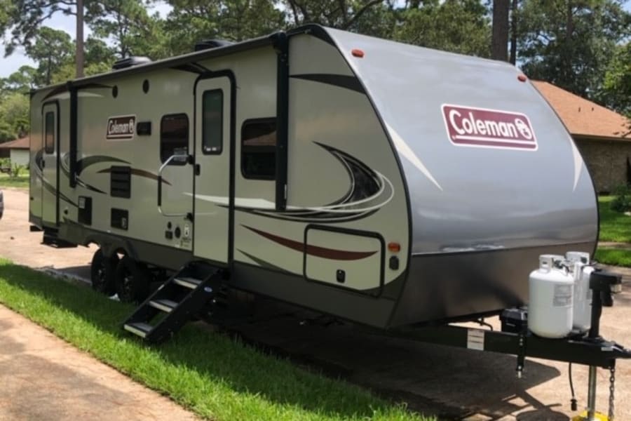 Modern light grey Coleman RV travel trailer, perfect for an RV rental adventure. Equipped with dual propane tanks and easy-access steps.