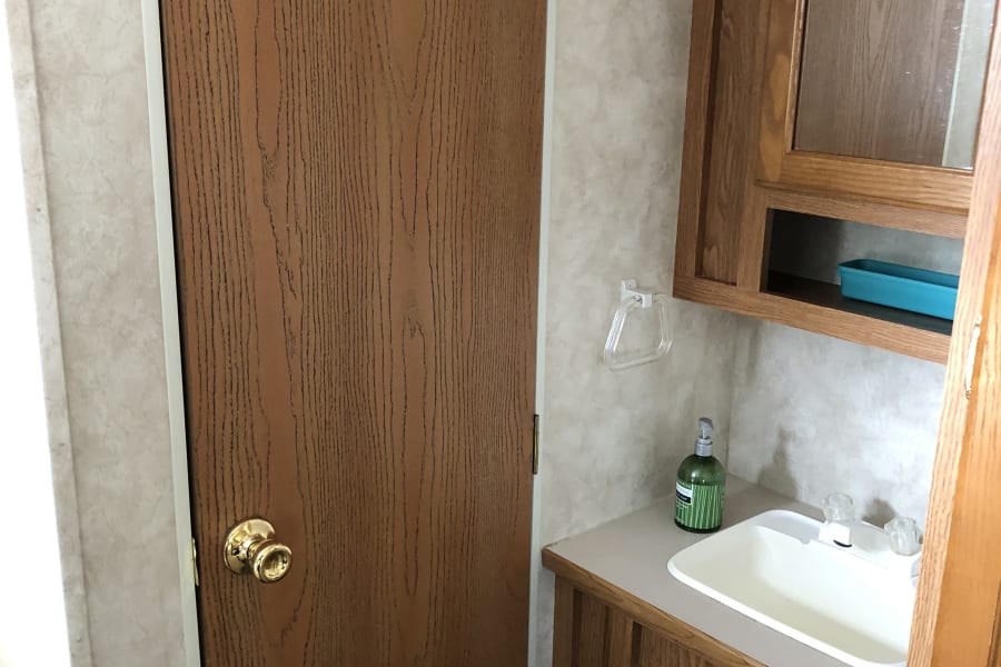 RV rental: a wooden door with brass knob, compact sink, and oak cabinets define this functional interior space.