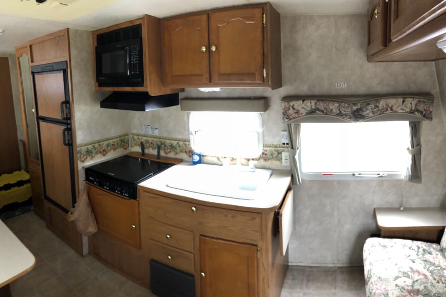 RV rental interior: Kitchen view with microwave, stove, sink, refrigerator, and wood cabinets.