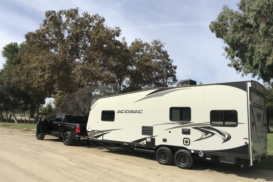 A black pickup truck towing a large white RV rental on a dirt lot, ready for your next travel or camping adventure.