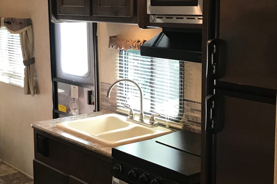 RV rental kitchen interior: sink, microwave, stove, fridge, and cabinets in a compact, well-equipped space.