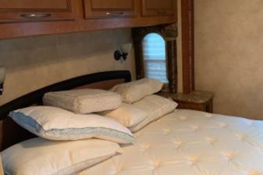 Comfortable RV rental bedroom featuring a large bed with plush pillows and overhead storage cabinets.