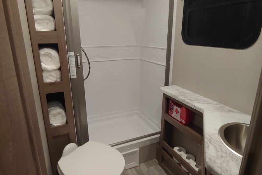RV rental bathroom featuring a toilet, stand-up shower, and vanity with sink, plus built-in storage for essentials.