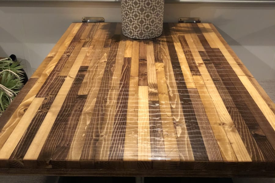 RV rental's custom wooden table and potted plant against ribbed blinds, offering a cozy and functional space.