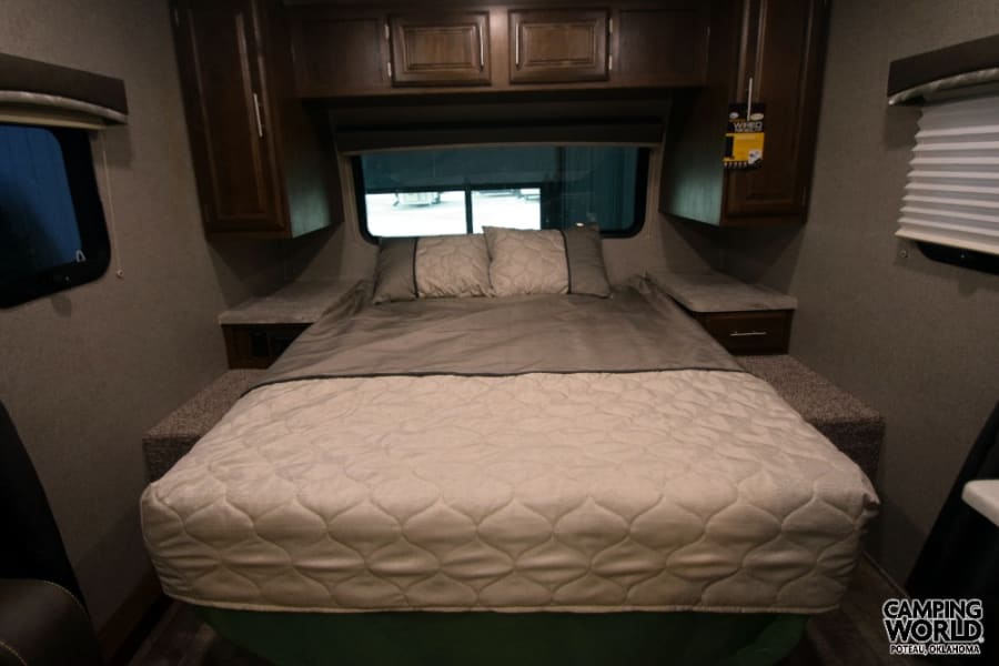 Explore a compact yet comfortable RV rental bedroom, featuring a neatly made bed, overhead cabinets, and windows.