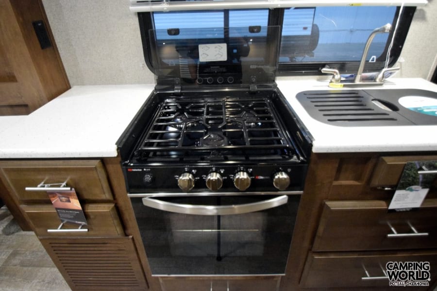 Modern RV rental kitchen with a black gas range, oven, sink, and white speckled countertop. Perfect for travel cooking.