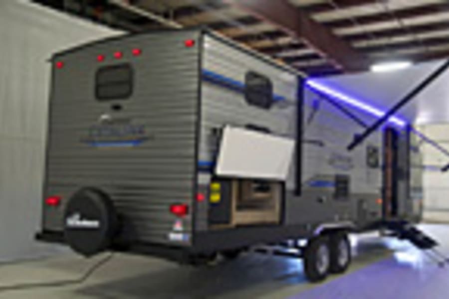 Gray travel trailer with an outdoor kitchen, extended awning & blue lights &ndash; perfect for your next RV rental trip!
