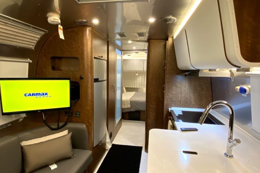 Modern RV rental interior: Kitchen, living area with TV, and hallway leading to a cozy bedroom setup.