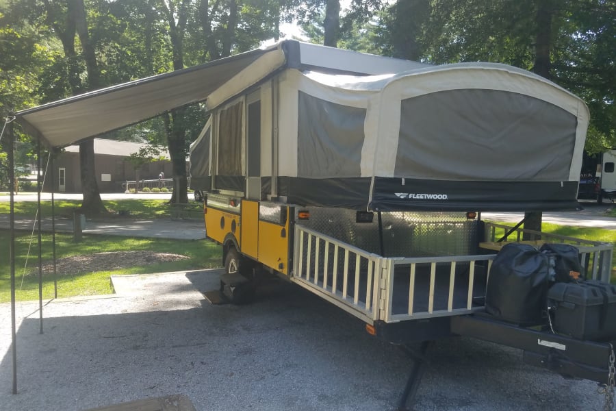 Yellow Fleetwood pop-up RV rental extended at a sunny campground for outdoor adventures.