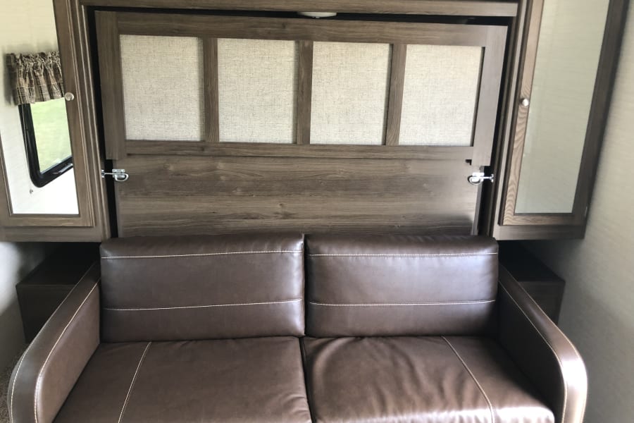 RV rental interior: Brown sofa, wall-mounted wooden Murphy bed, and side mirrored cabinets create a compact space.