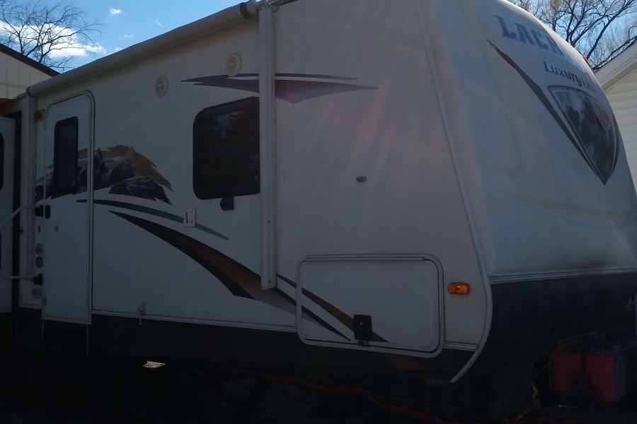 Bright sun shines on this white Laredo Luxury Lite RV, ideal for an rv rental. It's parked outdoors under a blue sky.
