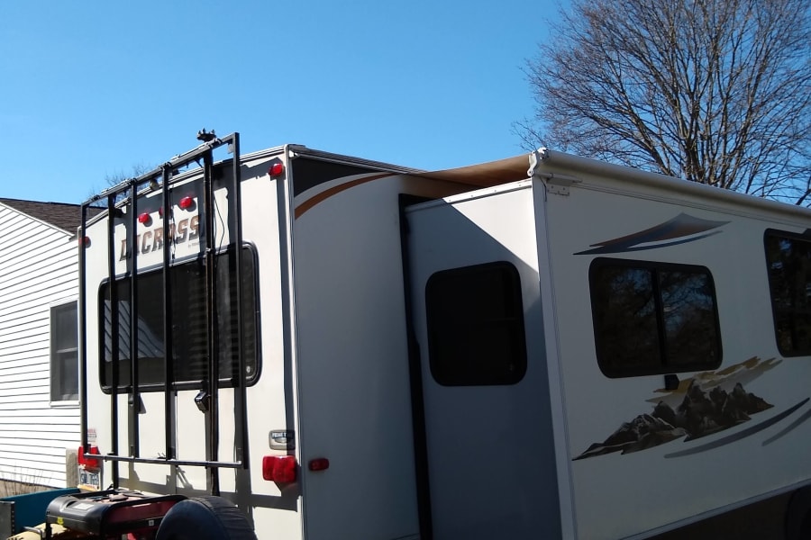 White Lacrosse travel trailer (RV rental) with slide-out extended, parked on gravel under a clear blue sky.