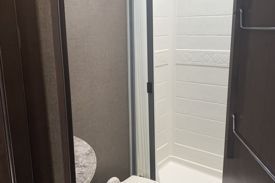 Explore this compact RV rental bathroom with a toilet, an enclosed stand-up shower, and a small vanity.