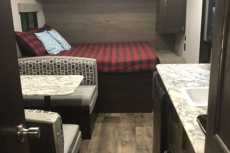 Cozy RV rental interior featuring a comfy bed, dinette, and kitchen. Perfect for your next travel trailer adventure!