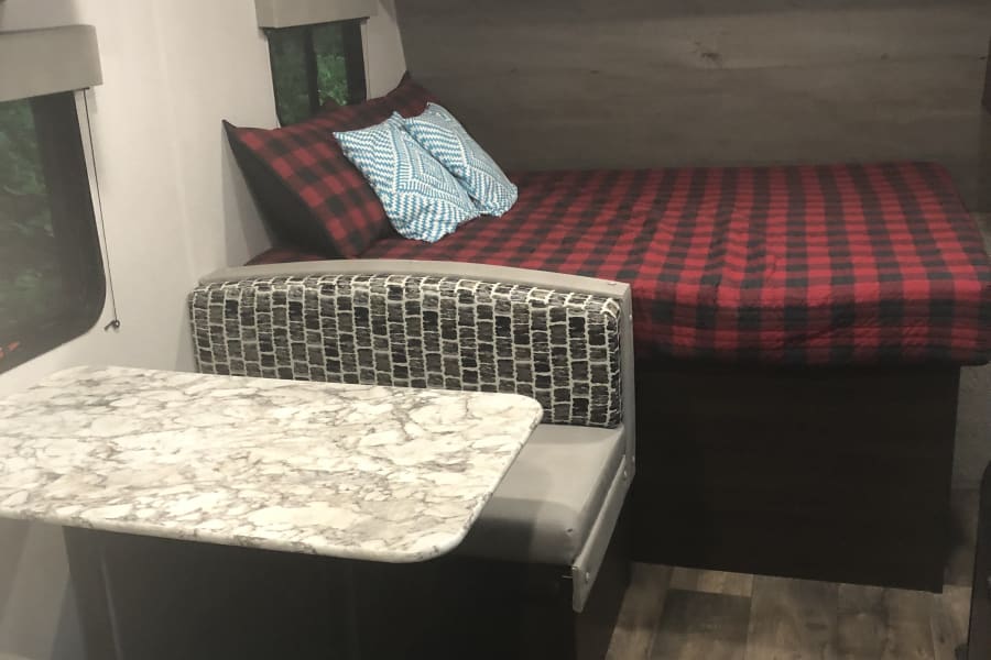 Cozy RV rental interior with dinette seating and a bed featuring a classic red buffalo check quilt.