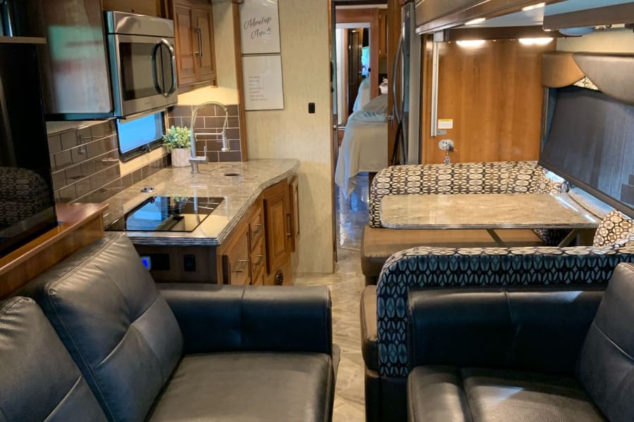 Inside a luxurious RV rental: features a full kitchen, comfy dining booth, and soft leather living area seating.