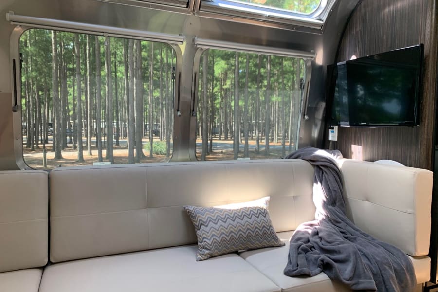Comfortable Airstream RV rental interior with a view of a peaceful pine forest campground. Ideal for nature lovers.