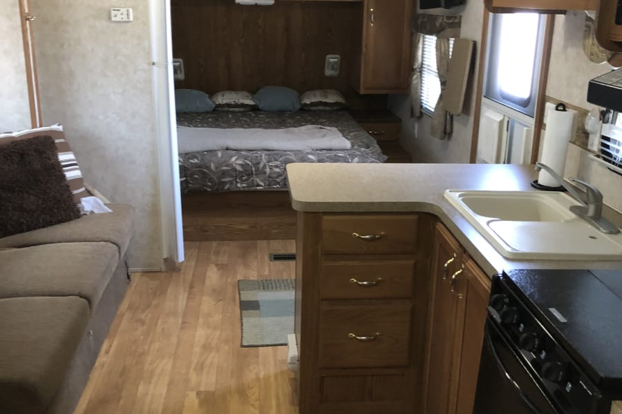 An RV rental's inviting interior: kitchen counter with sink, a cozy living area with couch, and a bedroom beyond.