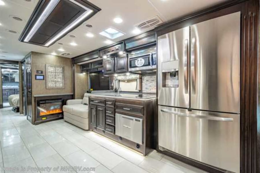 Luxury RV rental interior: spacious living area with modern kitchen, stainless steel appliances, and built-in fireplace.