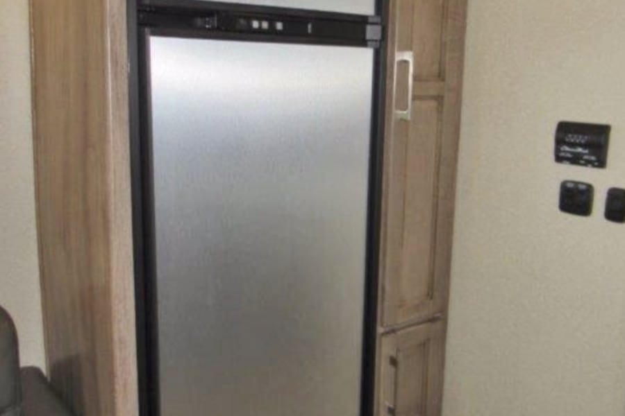 RV rental: Compact refrigerator with freezer, integrated into light wood cabinetry alongside storage. RV interior view.